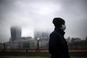 A man wearing a face mask walks past a view of the City of London which is covered in low mist (Victoria Jones/PA)