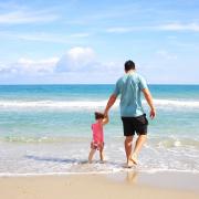 A father with his daughter walking on a beach (Canva)